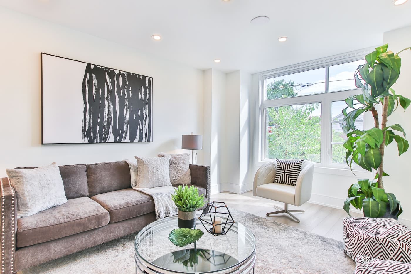 Living room with a light grey sofa, framed prints and a tall plant by the window