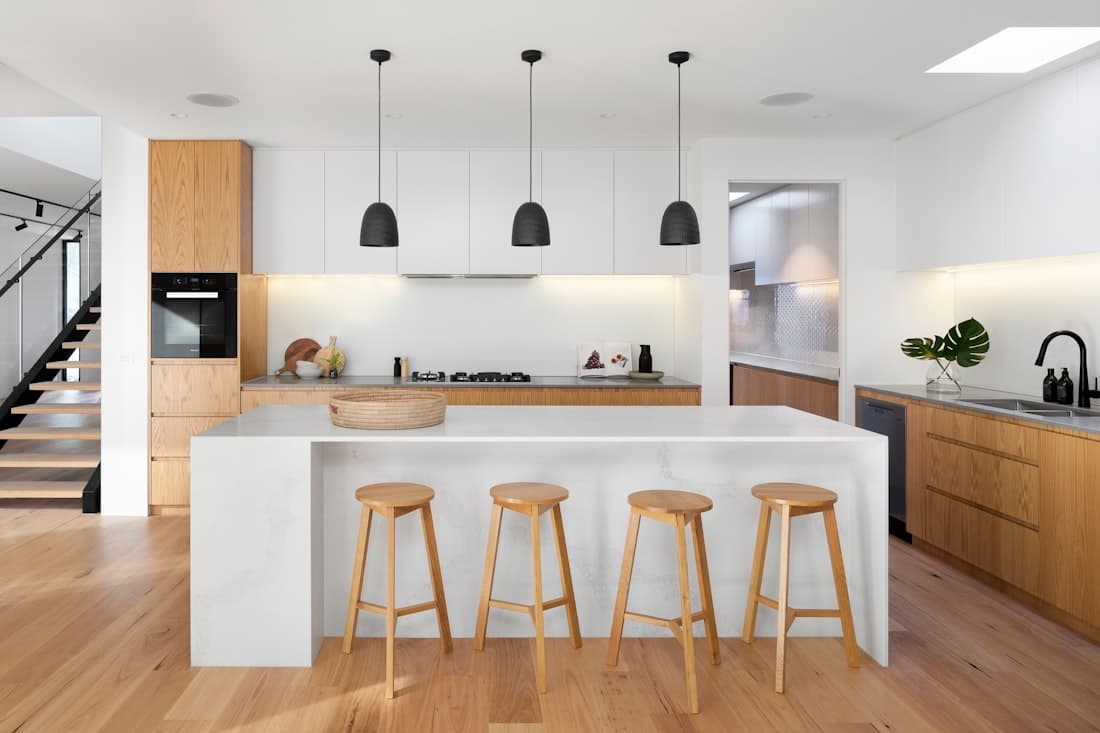 Kitchen with a white island, wooden stools and pendant lights